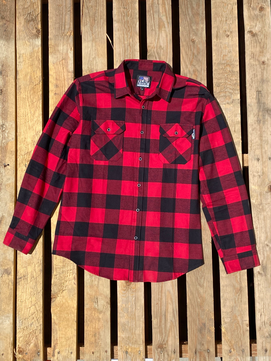 The Standard Freedom Flannel in red and black buffalo check laying on a pallet of wood. 