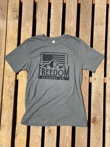Freedom Flannel basic logo tee shirt in heather green laying on pallet wood. 